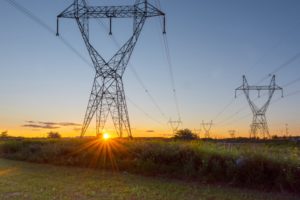 A row of tall power lines spread out across a green field at sunset
