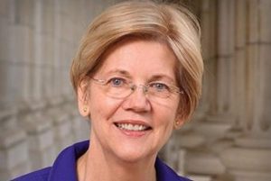 A WOMAN WITH SHORT BLONDE HAIR AND SPECTACLES SMILES INTO THE CAMERA